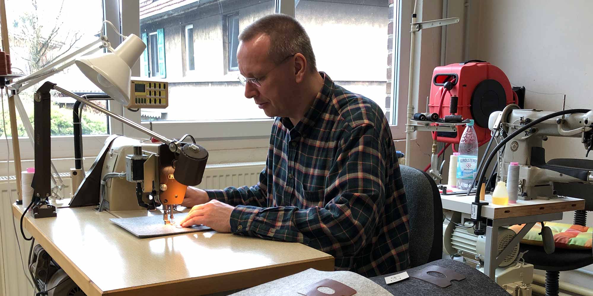 A man sits at a sewing machine and sews high-quality leather parts