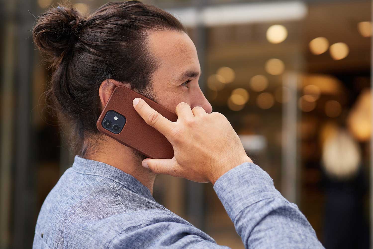 A man holds his iPhone 13 Pro Max with leather case to his ear and talks on the phone