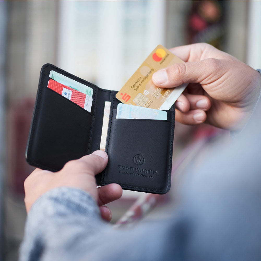 Offen gehaltene GOOD WILHELM BiFold Wallet aus schwarzem Vacetta-Leder mit sichtbaren Kartenfächern und RFID-Schutz.