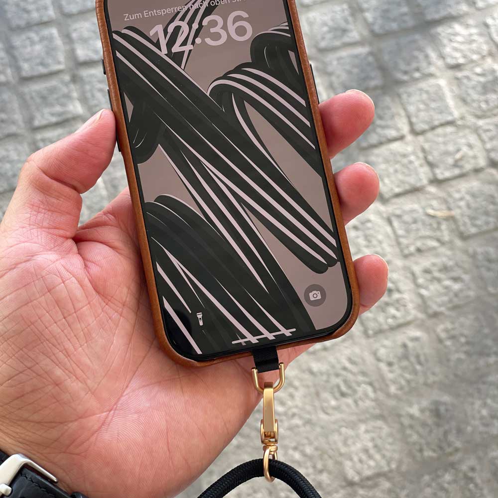Good Wilhelm Handykette Handyband schwarz mit goldenem Karabiner, Mann hält iPhone Hülle