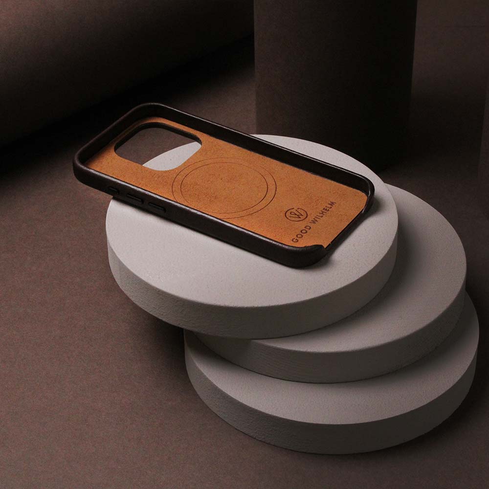 Brown iPhone case made of high-quality leather, lying on a table with decorative wooden disk underneath