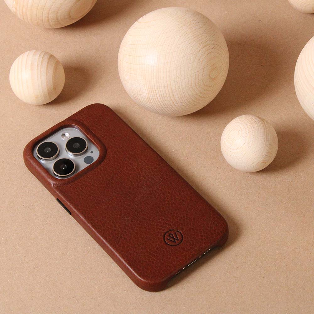 Brown iPhone case made of high-quality leather, lying on a table with decorative wooden balls in the background