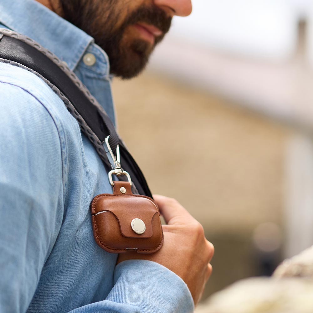 A leather Airpods Pro case hangs from a backpack with a snap hook