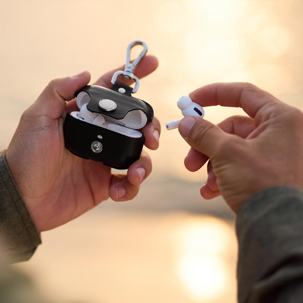 Two hands holding an opened leather Airpods case