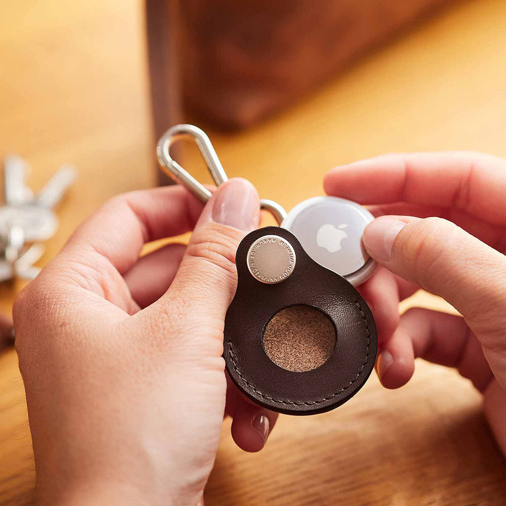 Two hands are about to push an Airtag from Apple into an Airtag case
