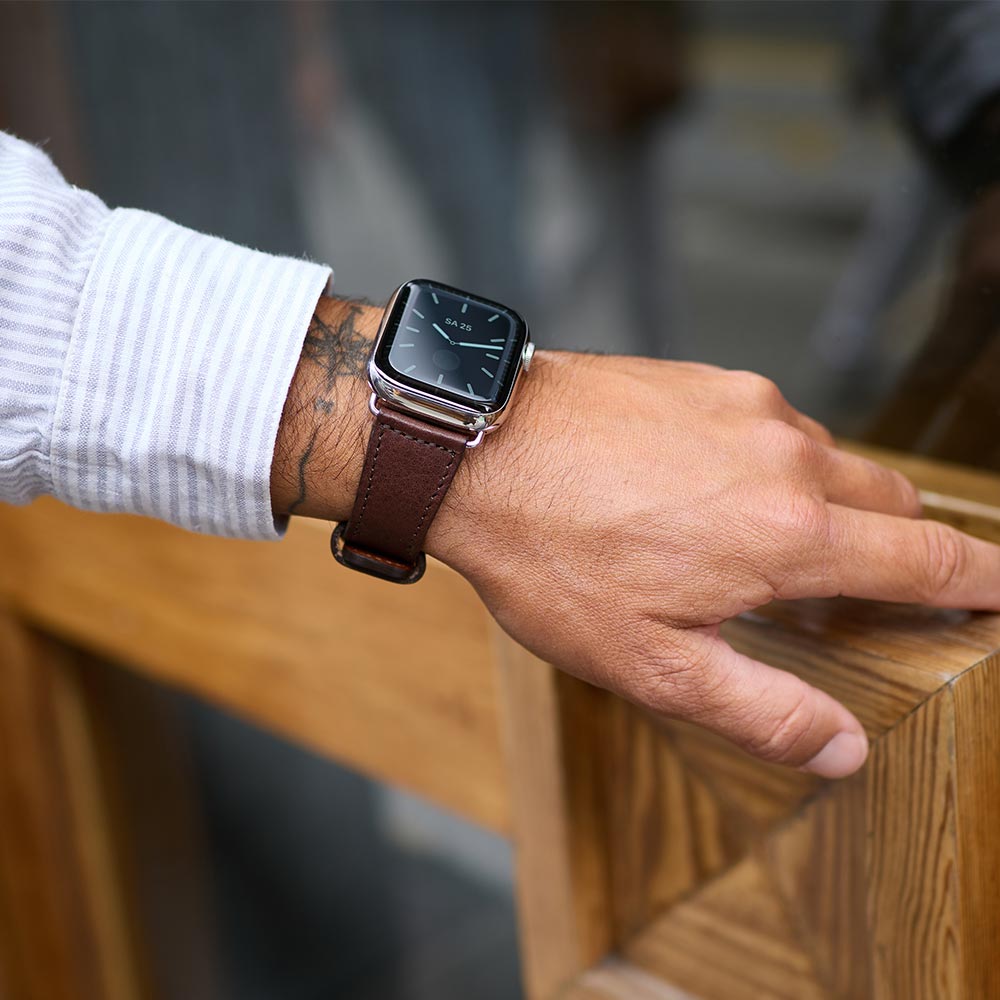 A man grips a door handle and shows his watch with a leather strap for the Apple watch