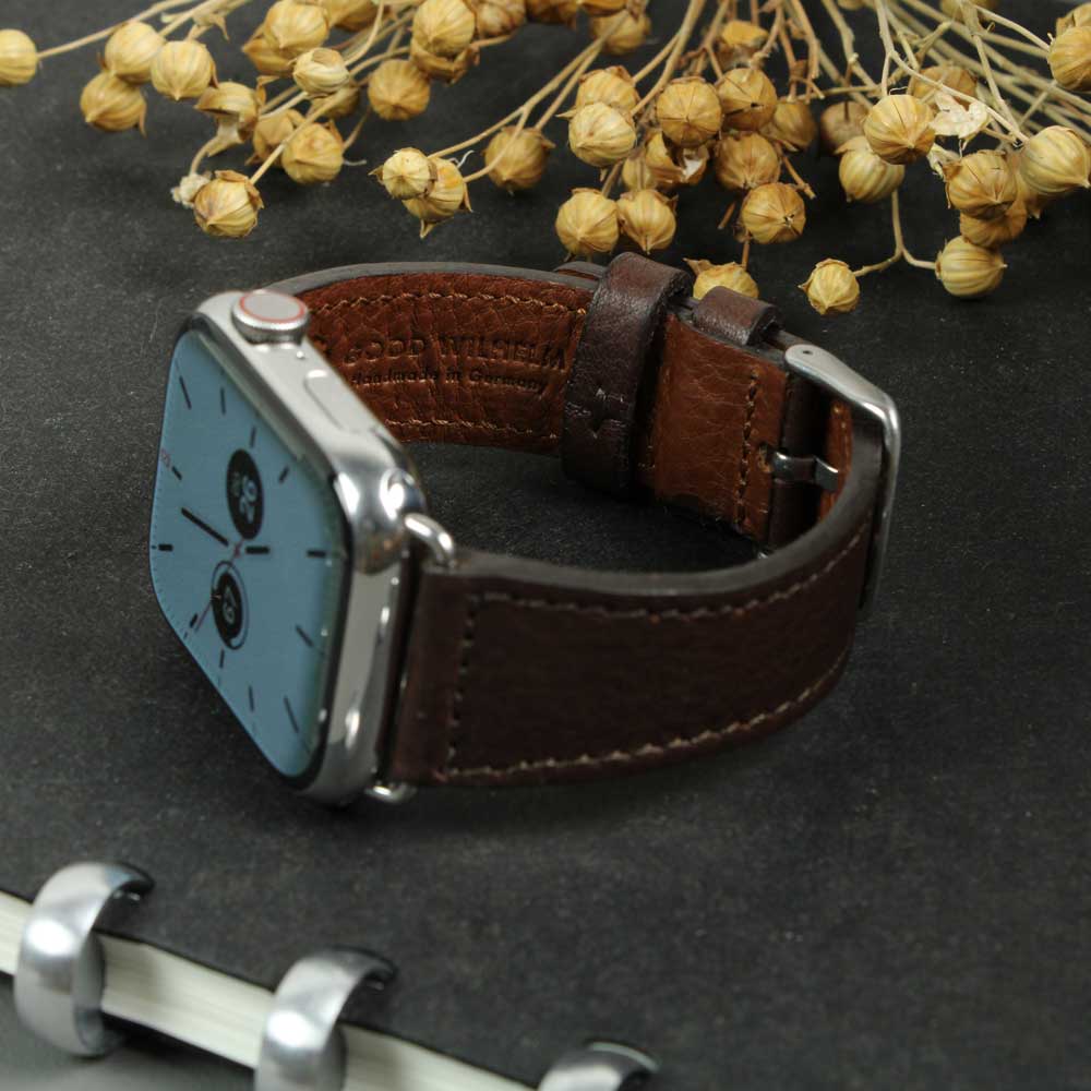 An Apple Watch with a dark brown leather strap lies on a table