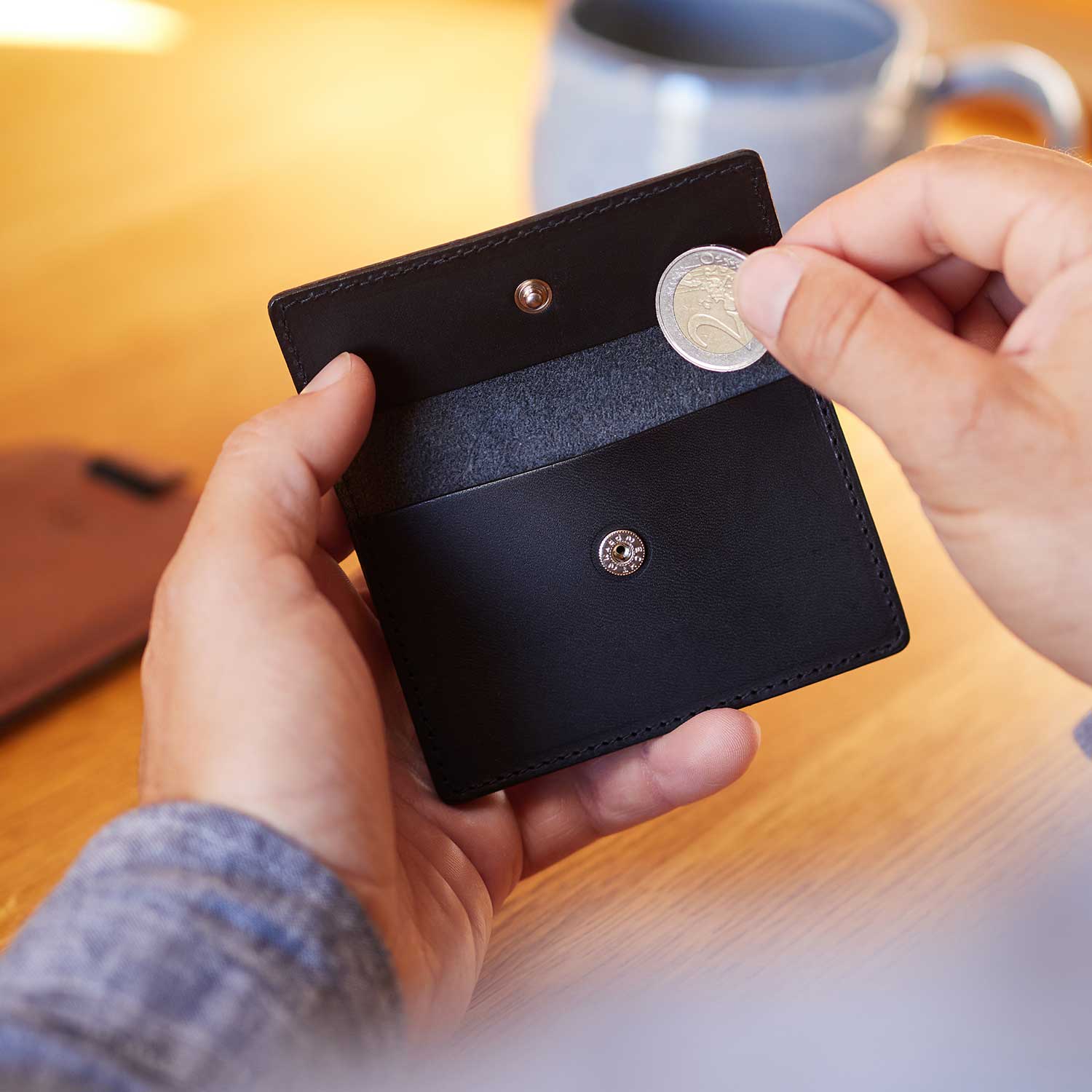 A man puts a coin into the coin compartment of the OTTO wallet in the color black by Goodwilhelm