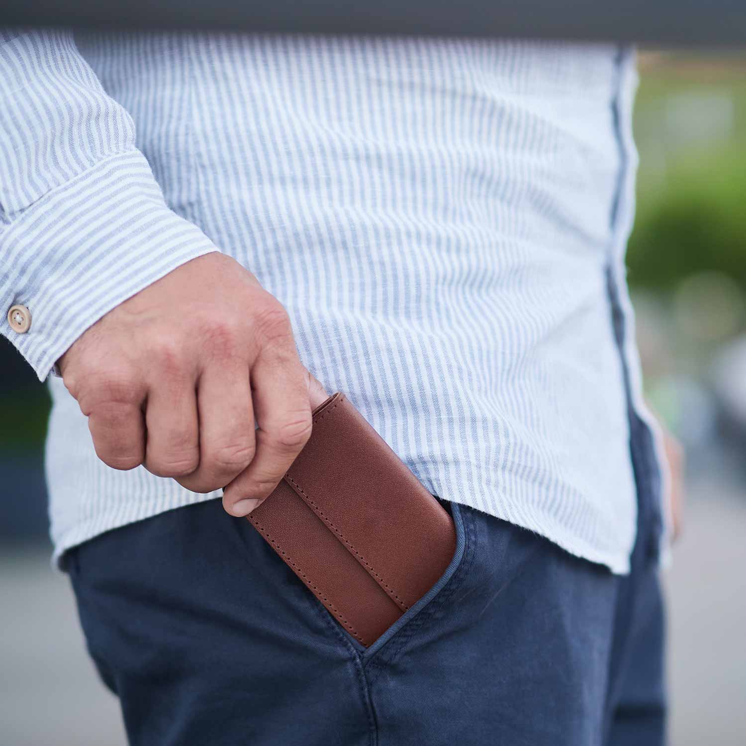 Man puts mini wallet OTTO by Goodwilhelm in the color cognac in his trouser pocket