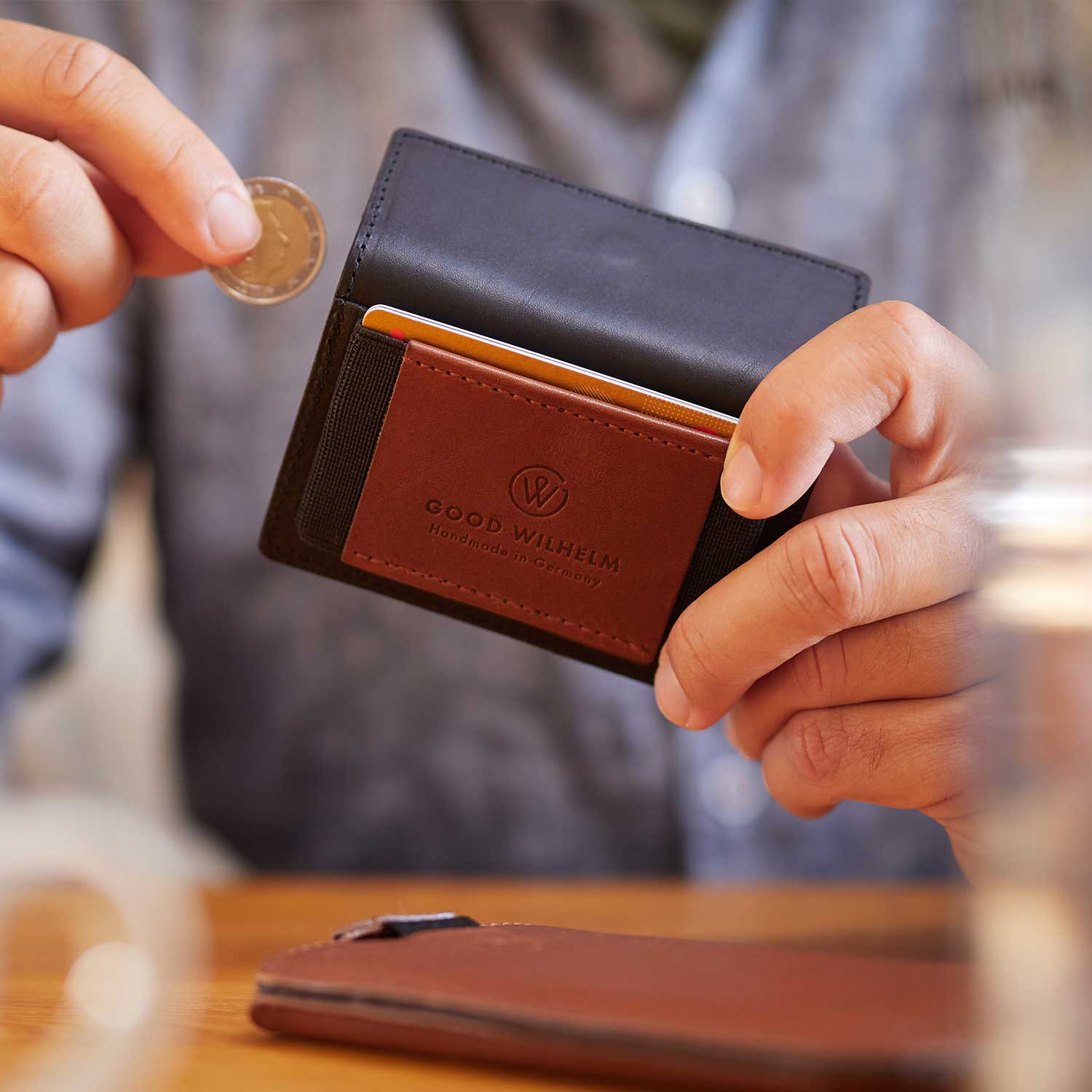 A man sits at a table and inserts a coin into a Goodwilhelm wallet