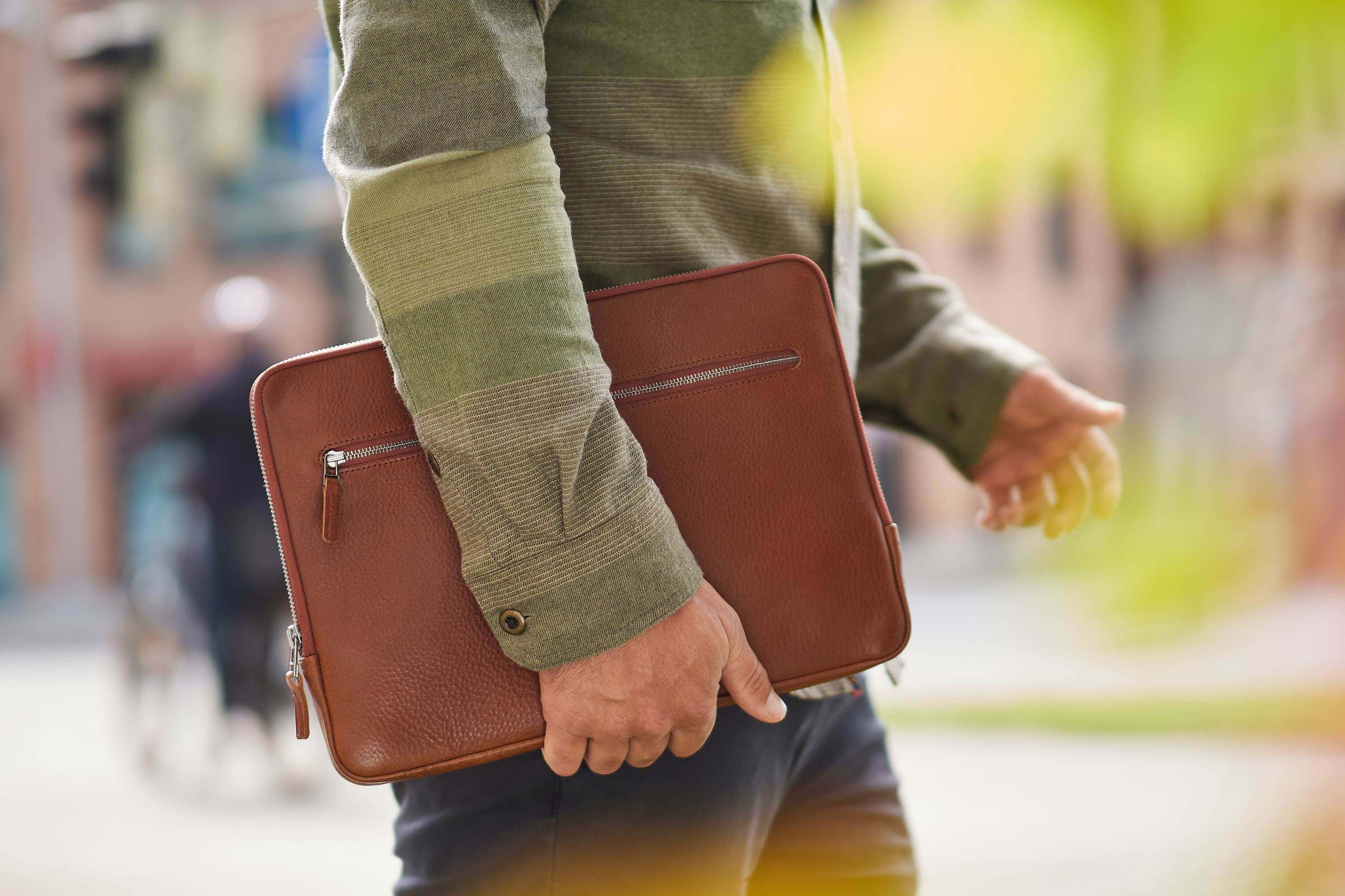 Ein Mann trägt eine Macbook Tasche aus Leder unter dem Arm
