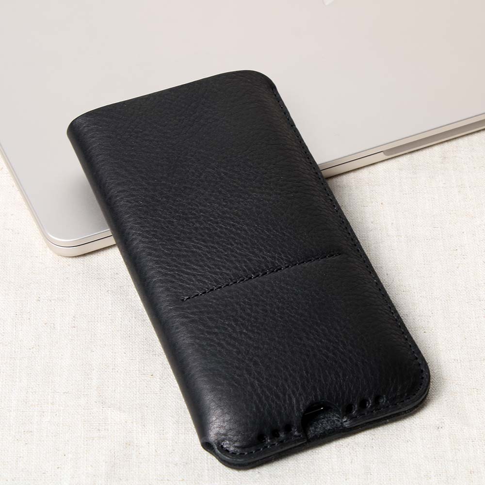 iPhone sleeve made of high-quality leather with charging recess and soundholes, based on a MacBook on a table - stylish protective case made of fine leather for optimum protection and functionality.