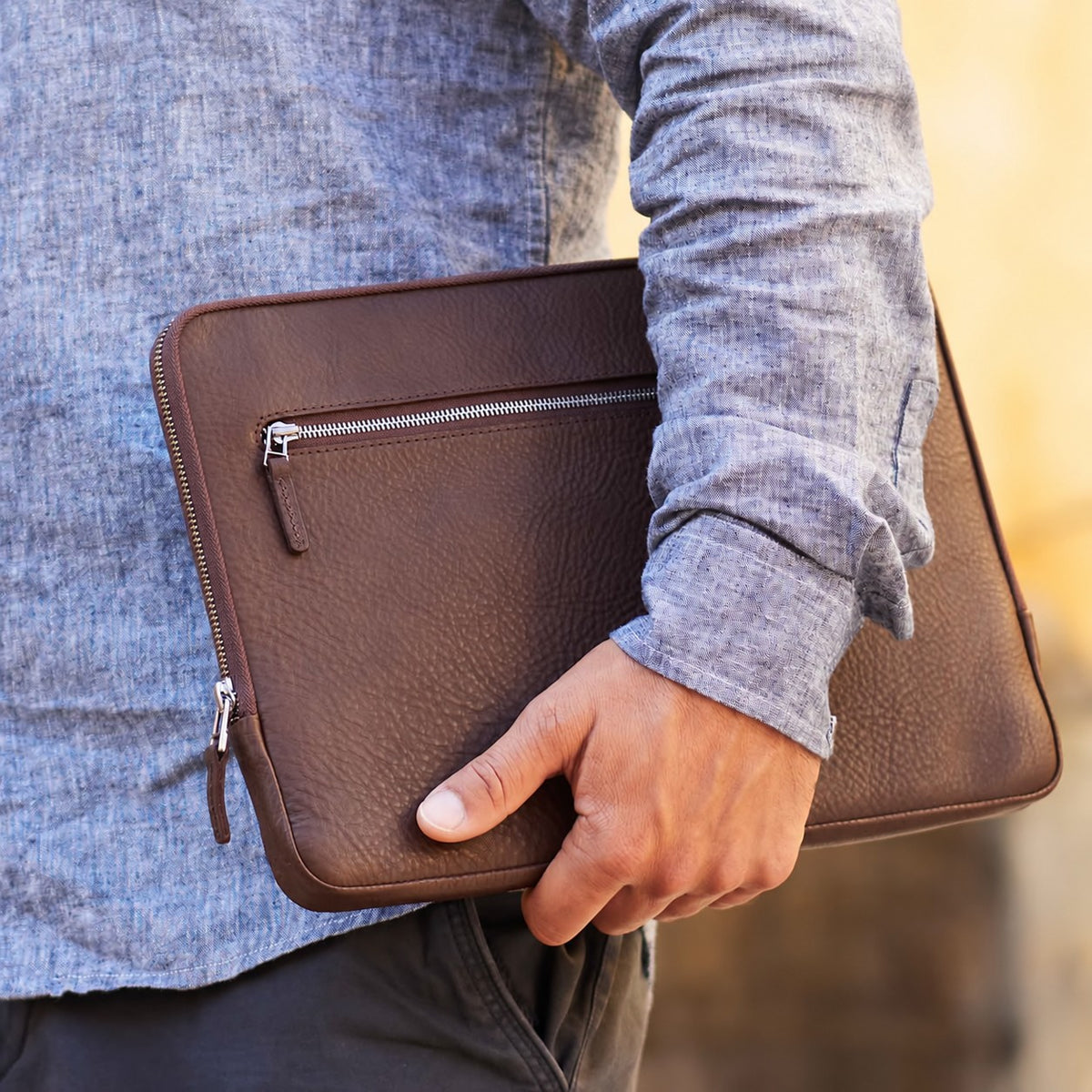 Ein Mann trägt unter dem Arm eine Good Wilhelm Macbook Pro Hülle aus dunkel braunem Leder