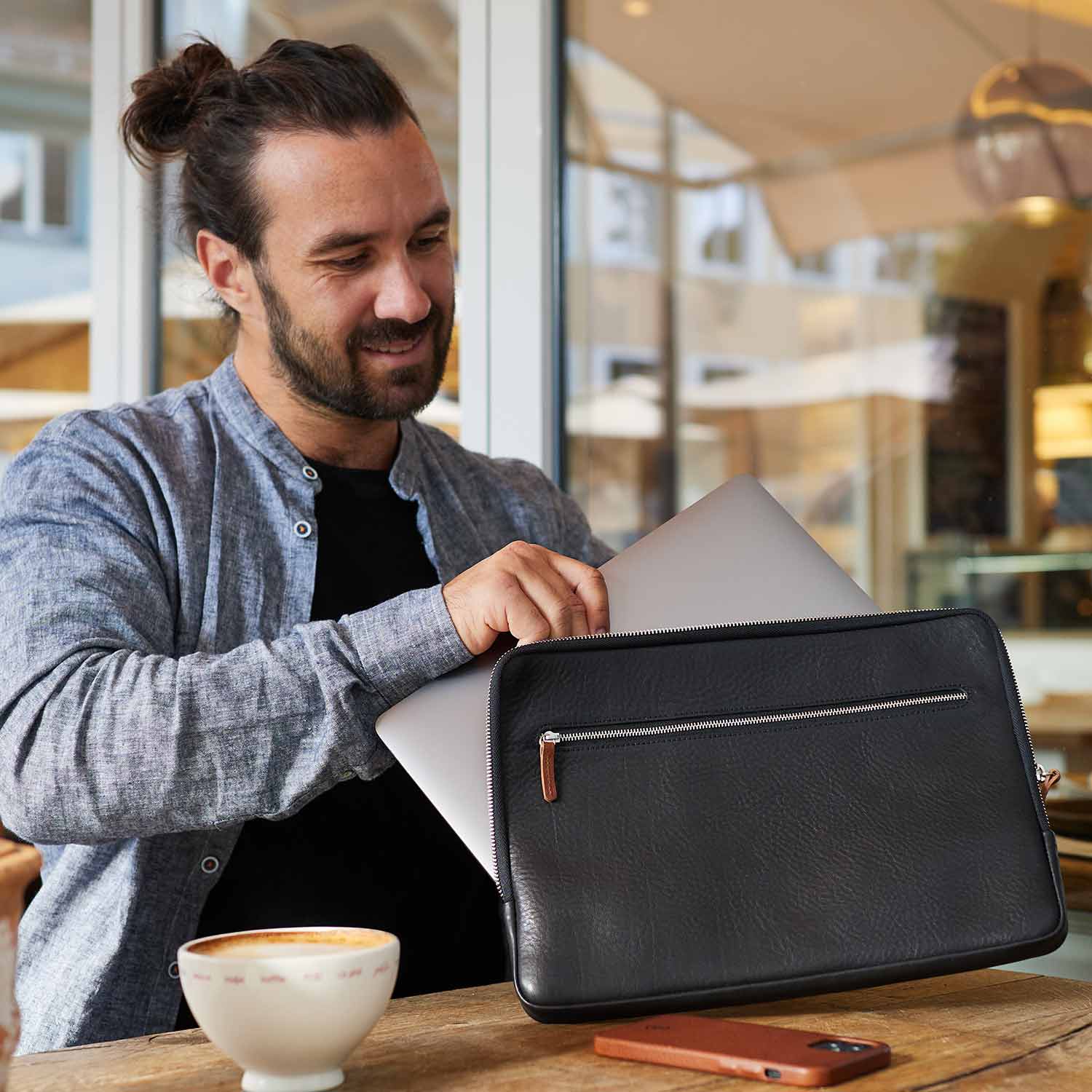 Ein Mann steckt ein Surface Laptop in eine schwarze Ledertasche von Good Wilhelm